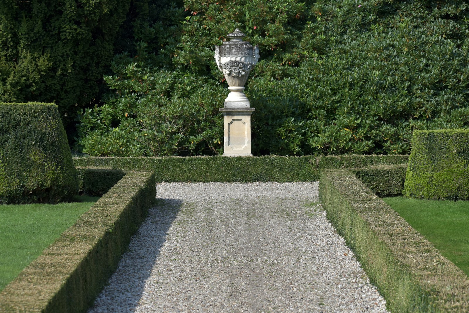 A garden with hedges and a statue in the middle